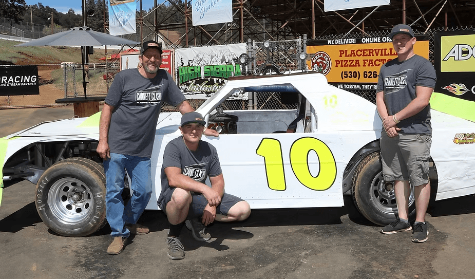 The Clash crew in Carnett Clash shirts beside a race car: Ted, Russ kneeling, and Forryst